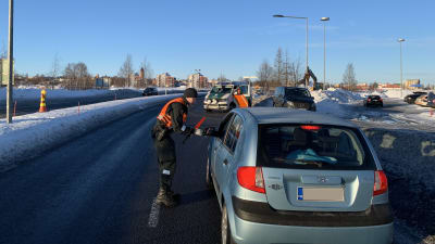 Några bilar i ett vintrigt landskap. En man i orange väst kontrollerar en ljusblå personbil som har stannat. 