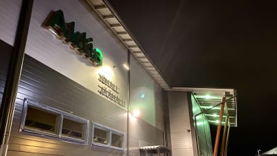 En grå hallbyggnad, kväll, byggnaden är upplyst. Raseborgs ishall. Det står Aktia ishall jäähalli på väggen.