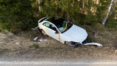 En vit personbil ligger i diket, den har fått stora skador både fram- och baktill.