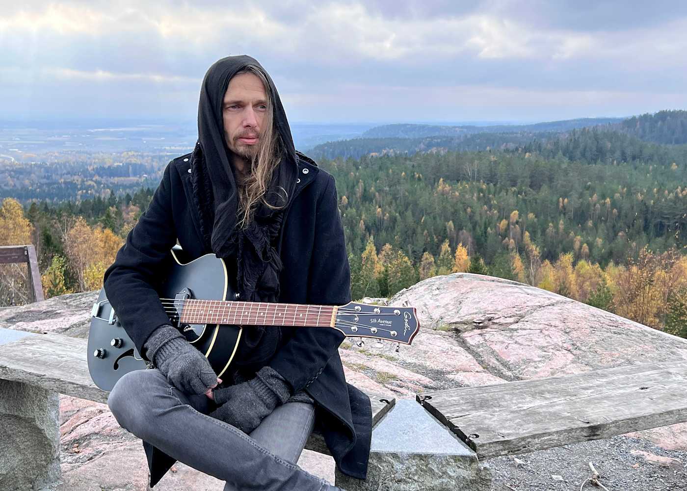 Juha Raivio kitaran kanssa kivellä kalliolla.