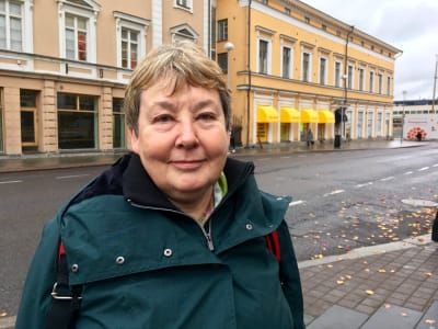 Merja Fredriksson poserar utomhus i höstväder. I bakgrunden syns ett gult hus. 