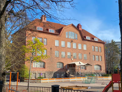 Ett stort skolhus. Huset kantas av skyddsstängsel.