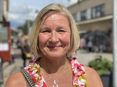 Glad kvinna i färgglad klänning står på gata i Pargas i solsken. 