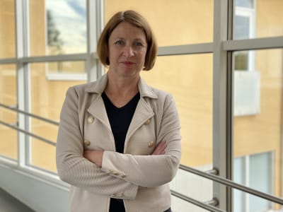Kvinna framför ett fönster, i bakgrunden ett gult hus.