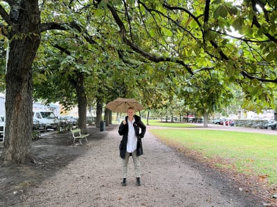 Fredrika Lindholm står och ler i en park. I handen håller hon ett paraply.