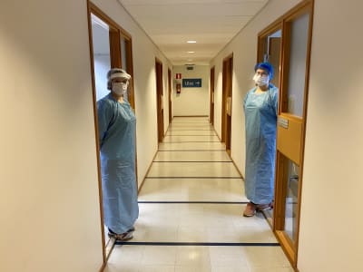 Två laboratorieskötare i skyddsdräkter står i var sin dörröppning i en korridor. 