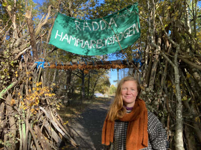 Sofia Olsson framför banderoll med texten rädda Hammarbyskogen
