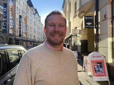 Ted Urho står och ler på en solig gata i Helsingfors centrum.