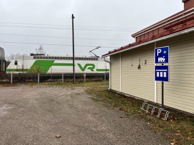 En parkeringsplats med p-skylt och cykelställ och ett tåg som kör förbi.