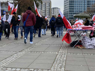 Människor vandrar på ett promenadstråk i Warszawa, många bär polska flaggor.