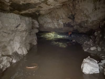 Johan Rikberg djupt inne i grottan, lyser med sin ficklampa. Stor vattenpöl i framgrunden. 