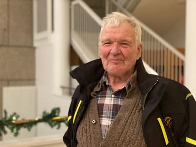 Äldre man i en aula med en trappa i bakgrunden.