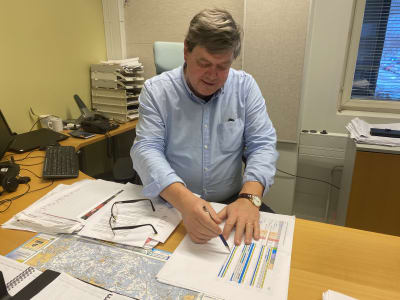 En man som sitter vid ett skrivbord och visar med pennan på några papper.