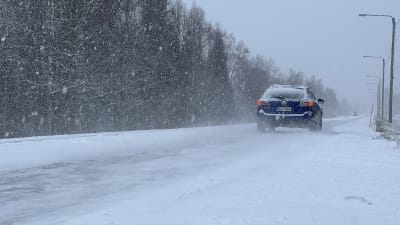Personbil som kör på en snöig väg i snöfall. 