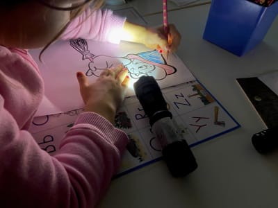 En flicka ritar i skenet av ficklampsljus.