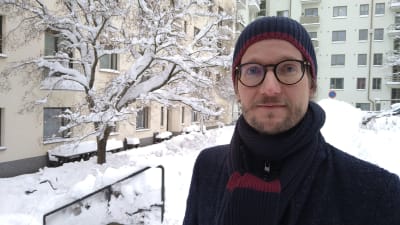 Man i glasögon och vinterkläder på en snöig innergård.