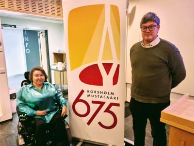 En kvinna i rullstol och en stående på var sin sida om en rollup