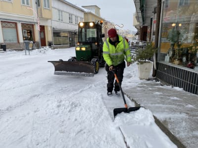 En man som skottar bort snö från en trappa längs en gågata.