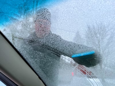 Mies skrapaa auton tuulilasia lumesta.