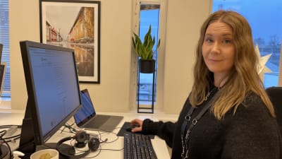 En kvinna med långt ljust hår sitter vid en dator vid ett skrivbord