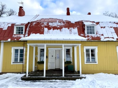 Ingången till ett gult trähus med rött tak. Det är snö på marken.
