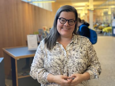 En glad mörkhårig kvinna som står i ett bibliotek.