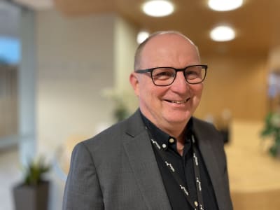 En glad man med glasögon och kavaj tittar rakt in i kameran. 