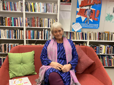 En leende gråhårig kvinna framför en bokhylla.
