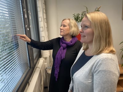 Lisbeth Hemgård och Annette Tallberg-Haahtela vid ett fönster. Lisbeth pekar utåt. 