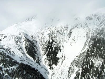 En snötäckt alpsluttning där toppen av berget är höljt av moln.