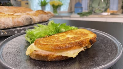 En stekt varm smörgås fylld med ost och skinka, med lite grönsallad på sidan av.