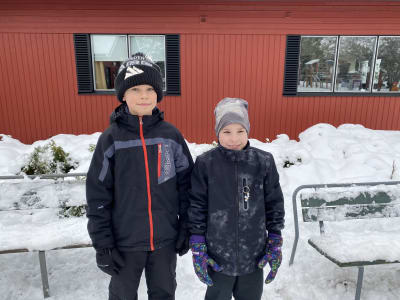 Två pojkar framför ett rött hus och massor med snö.