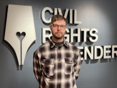 En skäggig man i 30 årsåldern med allvarlig och vänlig blick står framför texten Civil Rights Defenders