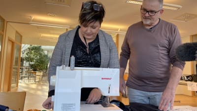 En man och en kvinna står böjda över en symaskin.