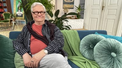 Professori ja unitutkija Markku Partinen istuu sohvan päällä ja katsoo hymyillen kameraan.