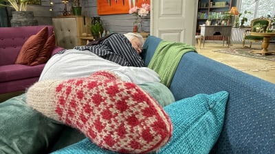 Markku Partinen makaa kyljellään sohvalla nukkuen punavalkoinen villasukka etualalla.
