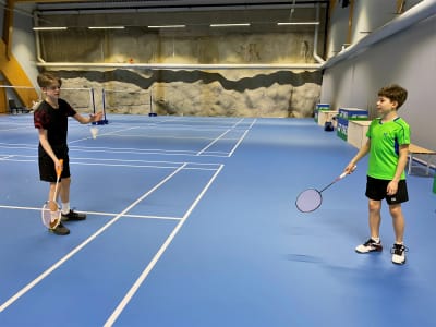 Två pojkar står på varsin sida av bilden och slår en badmintonboll mellan sig.