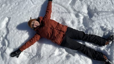 Ida Berg makaa lumen päällä ja tekee lumienkeliä.