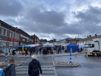 Marknad med torgförsäljning i Kristinestad. Människor rör sig i centrum av staden, det är regnvått.
