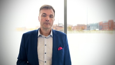 Personporträtt på Stefan Damlin. Han står med fönster bakom sig, är klädd i skjorta och kavaj, ser allvarlig ut.