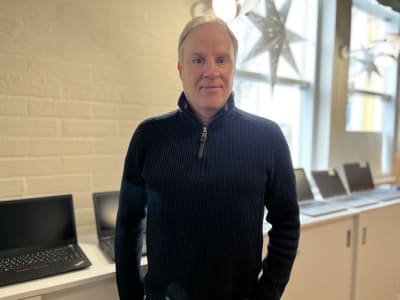 Man i 50-60-årsåldern står framför en rad bärbara datorer och tittar in i kameran.