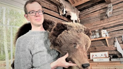 En man med glasögon håller en björnpäls över sin axel. 