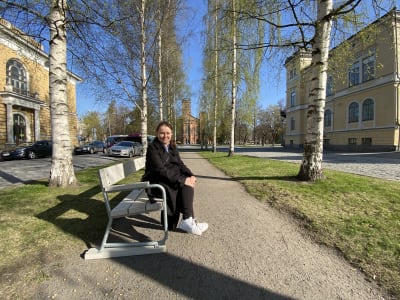 Kvinna sitter på parkbänk i esplanad
