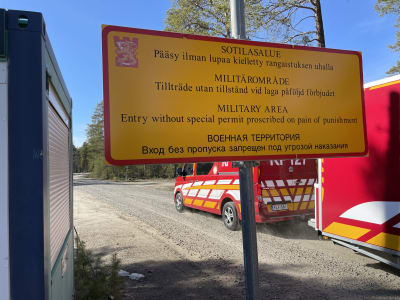 En skylt som informerar om att det är förbjudet att röra sig på militärområdet utan tillstånd. I bakgrunden räddningsverkets fordon. 