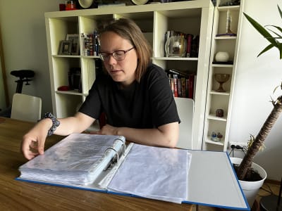 En kvinna sitter vid ett bord och bläddrar i en mapp med papper. 