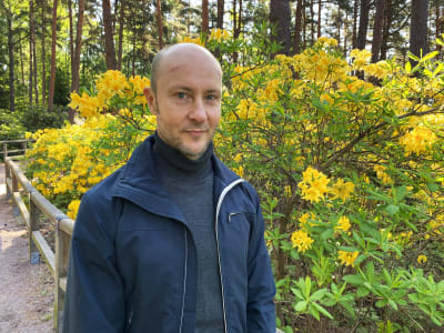 En man står framför en stor, gulblommande buske. 