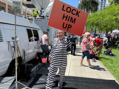En person i svart vit fängelserdräkt som håller i ett plakat med texten: "Lock him up"