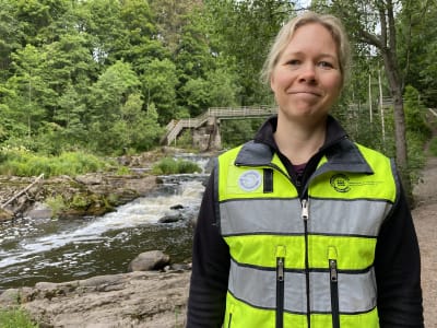 En kvinna i neonfärgad väst vid ett vattendrag.