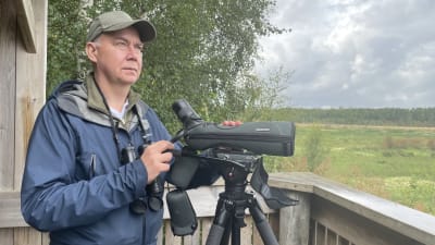 En man med keps står i ett fågeltorn med en tubkikare