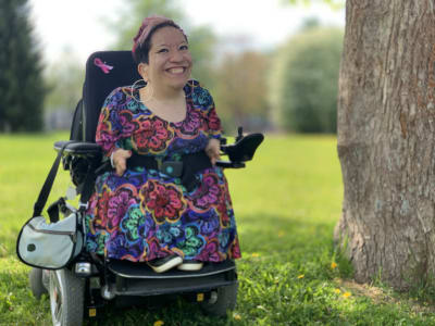 Anna Caldén i rullstol i en grön park intill ett träd. 